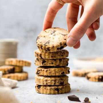 A stack of five vegan shortbread biscuits being picked up by a hand.
