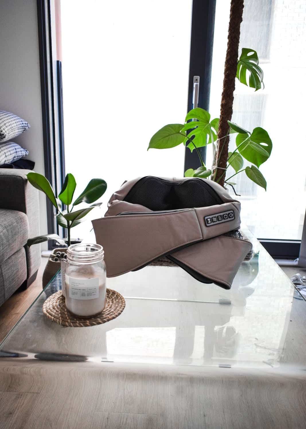 A back massager placed on a low glass table with a couple of plants and a candle next to it.