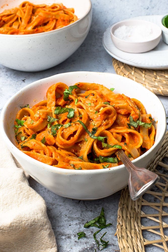 A bowl full of red pasta with a fork in it.