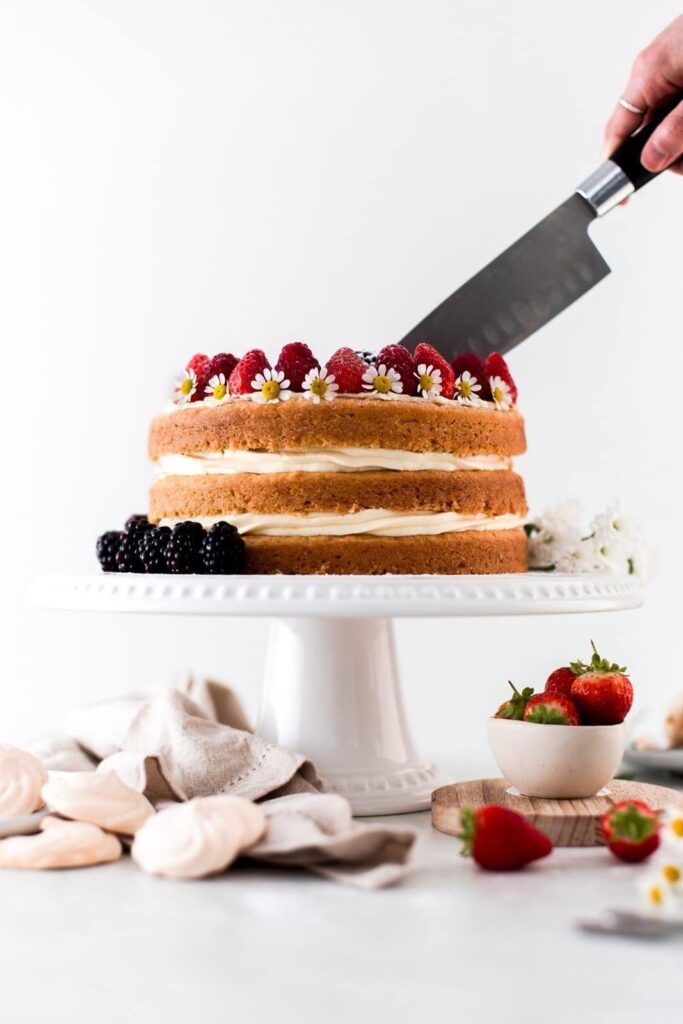 A knife cutting into a cake on a white stand. 