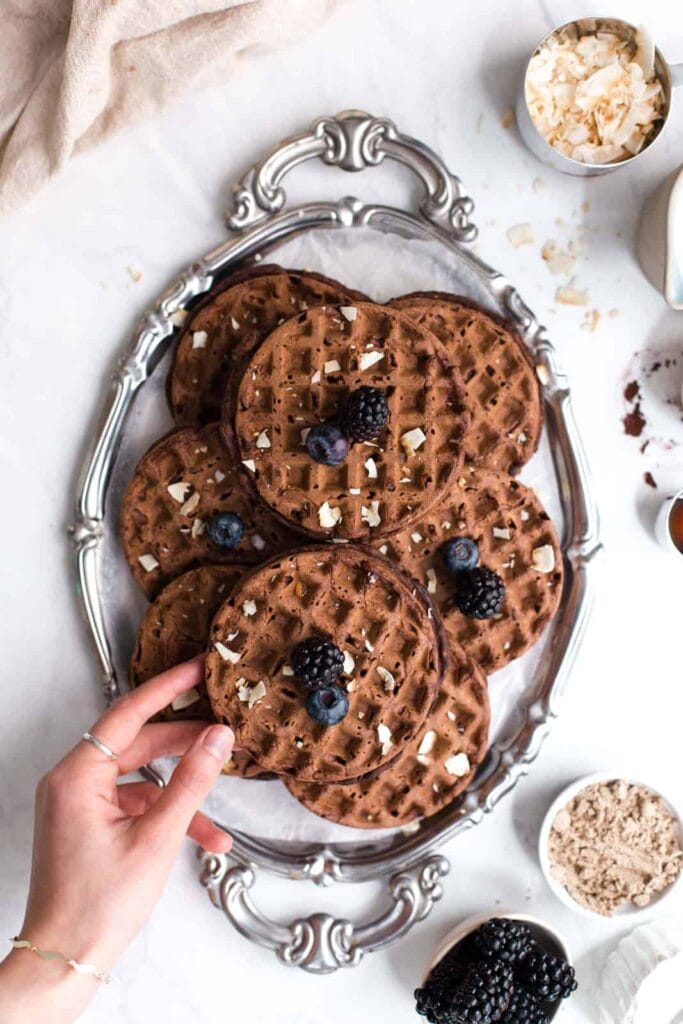 A hand reaching for chocolate waffles on a large silver tray