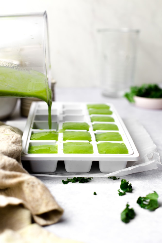 An action shot of green smoothie being poured into an ice cube tray. 