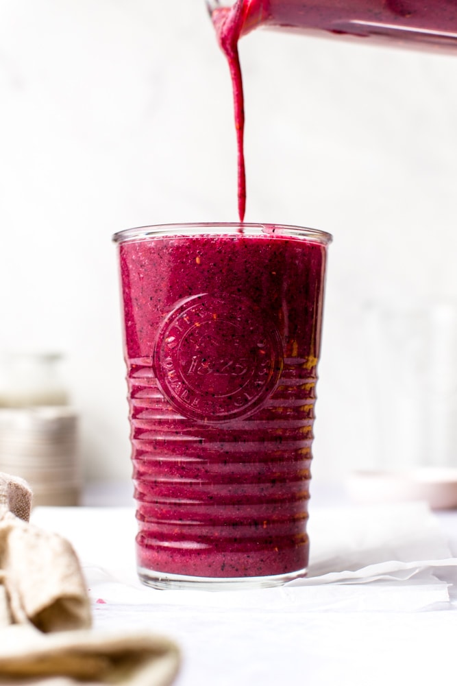 Raspberry and blueberry smoothie being poured into a large class on a white background. 