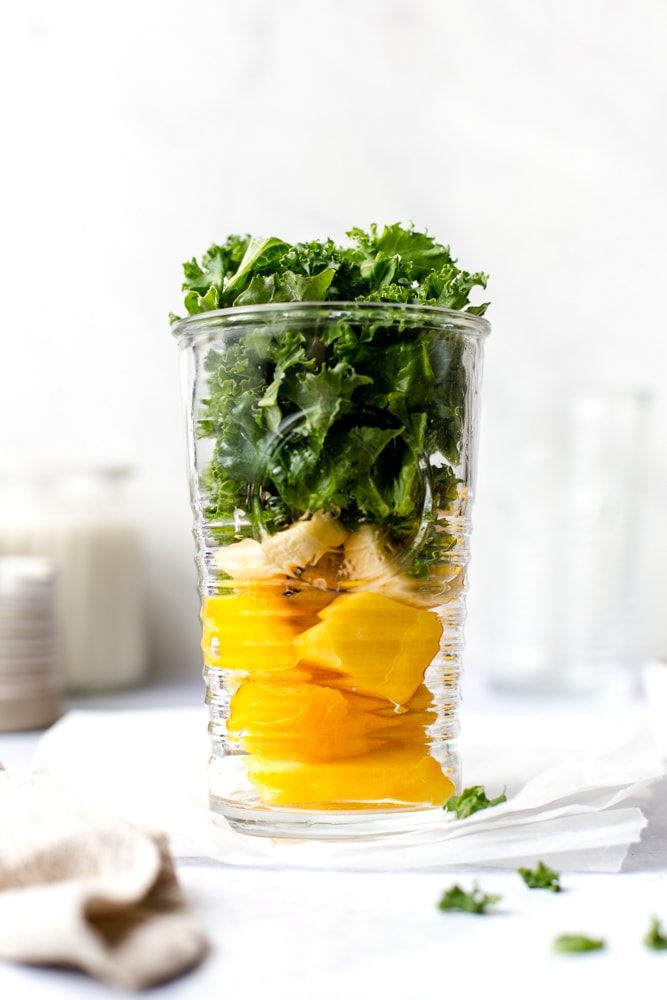 All the ingredients needed to make a mango and kale smoothie in a glass. 