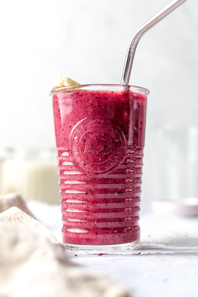 A glass full of red mixed fruit smoothie in a glass. 