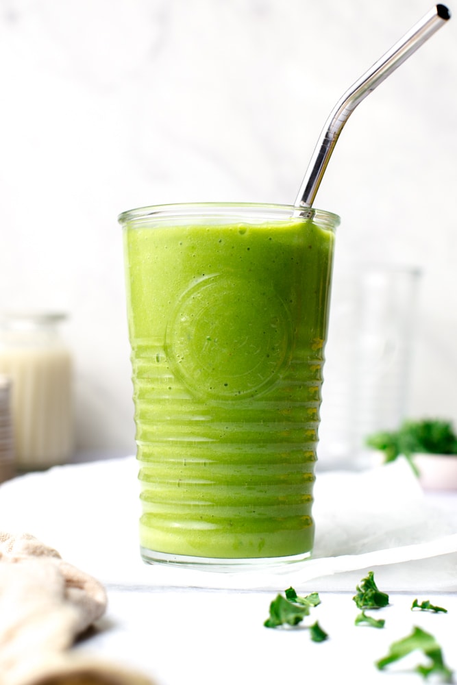 A glass containing green smoothie with a stainless steel straw.