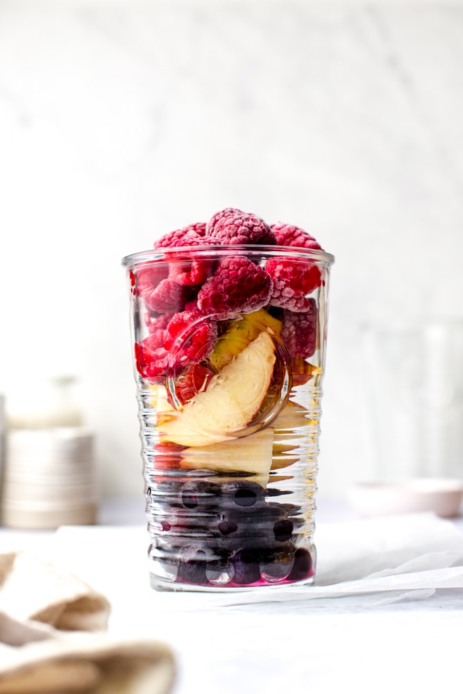 A glass full of ingredients needed to make a raspberry and blueberry smoothie. 