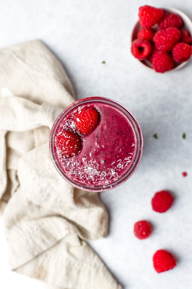 A close-up overhead view of raspberry smoothie with raspberries scatted around. 