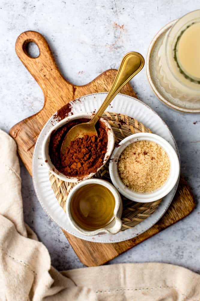 All ingredients needed to make oat milk hot chocolate laid out on a wooden board. 