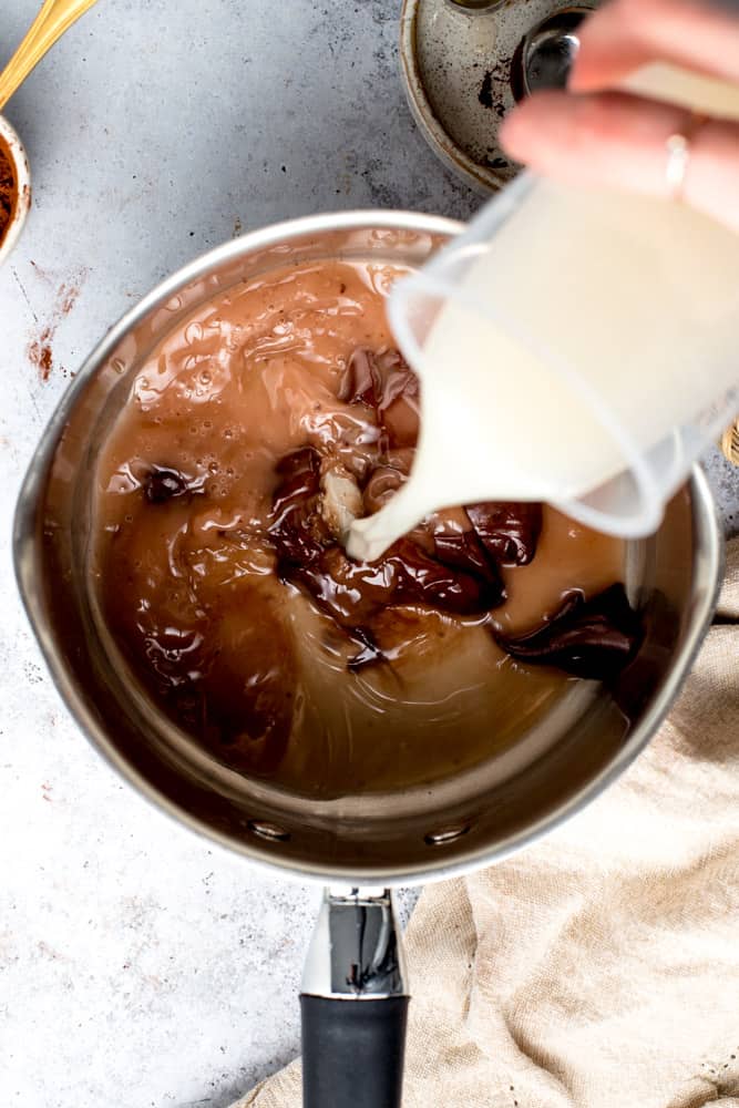 Oat milk being poured over a vegan hot chocolate mix into a small metal pan. 