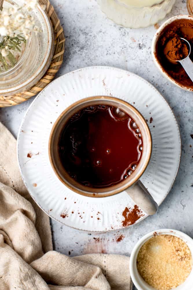 Overhead view of oat milk hot chocolate in a mug surrounded by cocoa ingredients. 