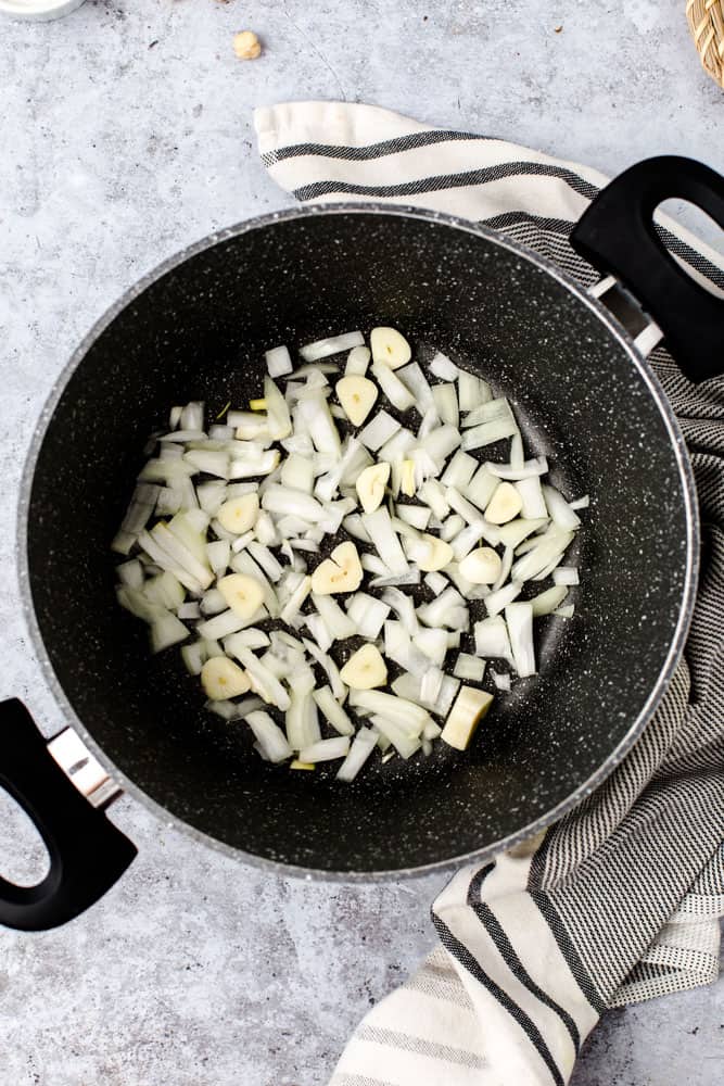 A marble cooking pan containing cut raw onion and garlic. 