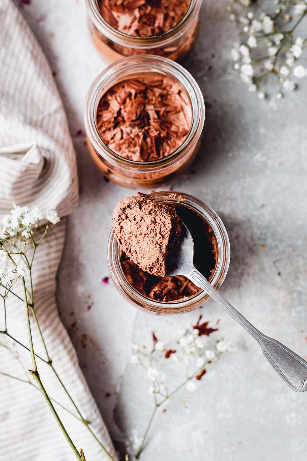 A spoon with vegan chocolate mousse placed on top of a jar. 
