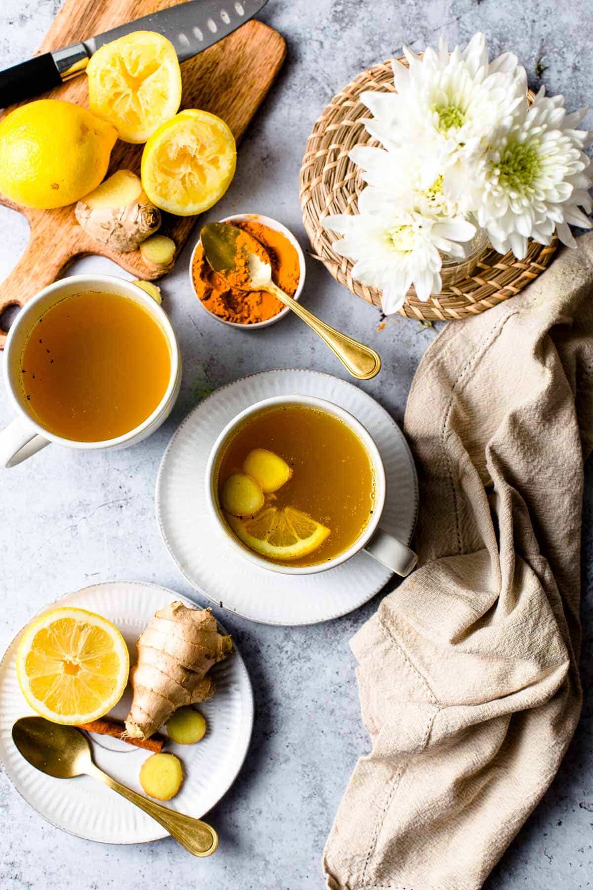 Two cups of cinnamon ginger tea surrounded by pieces of lemon, cinnamon and a small bouquet of flowers. 