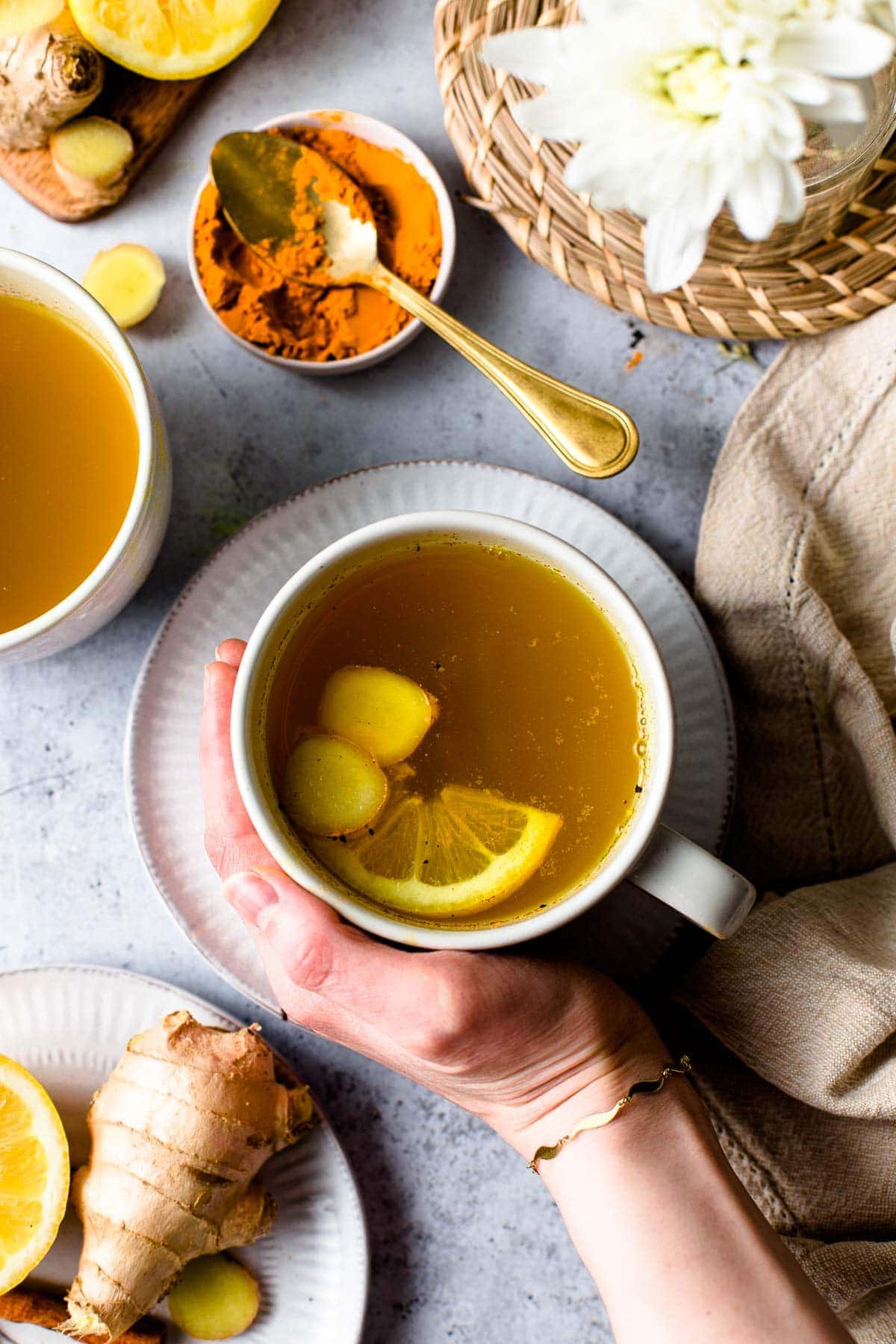 A hand holding a mug of cinnamon ginger turmeric tea placed on a table setting. 
