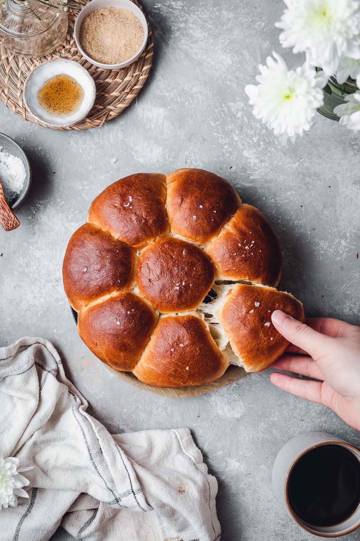 An overhead view of dinner rolls with one hand pulling apart one roll.