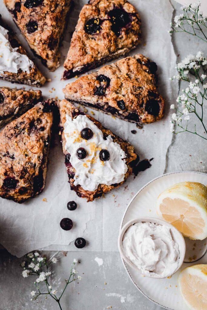 A close-up images of blueberry vegan scones, with one slice topped with coconut cream. 