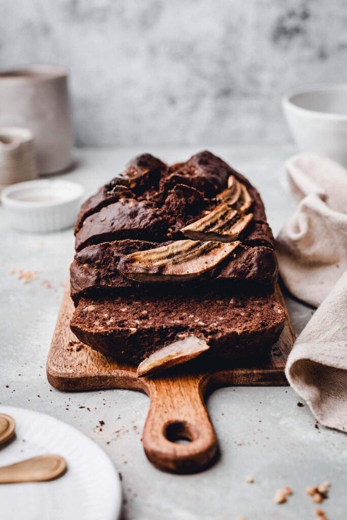 A side view of sliced chocolate bread loaf on a small wooden chopping board. 