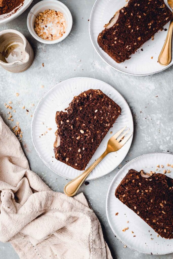 Slices of chocolate bread laid out on three small plates surrounded by forks and a napkin.