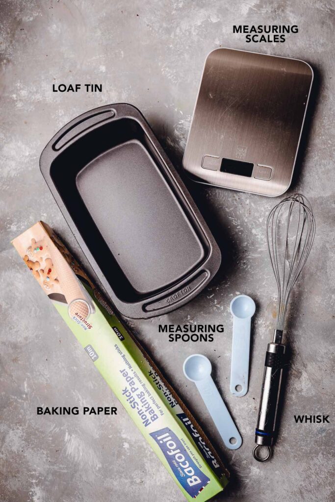 Various baking equipment like measuring spoons, scales and a tin on a flat surface. 