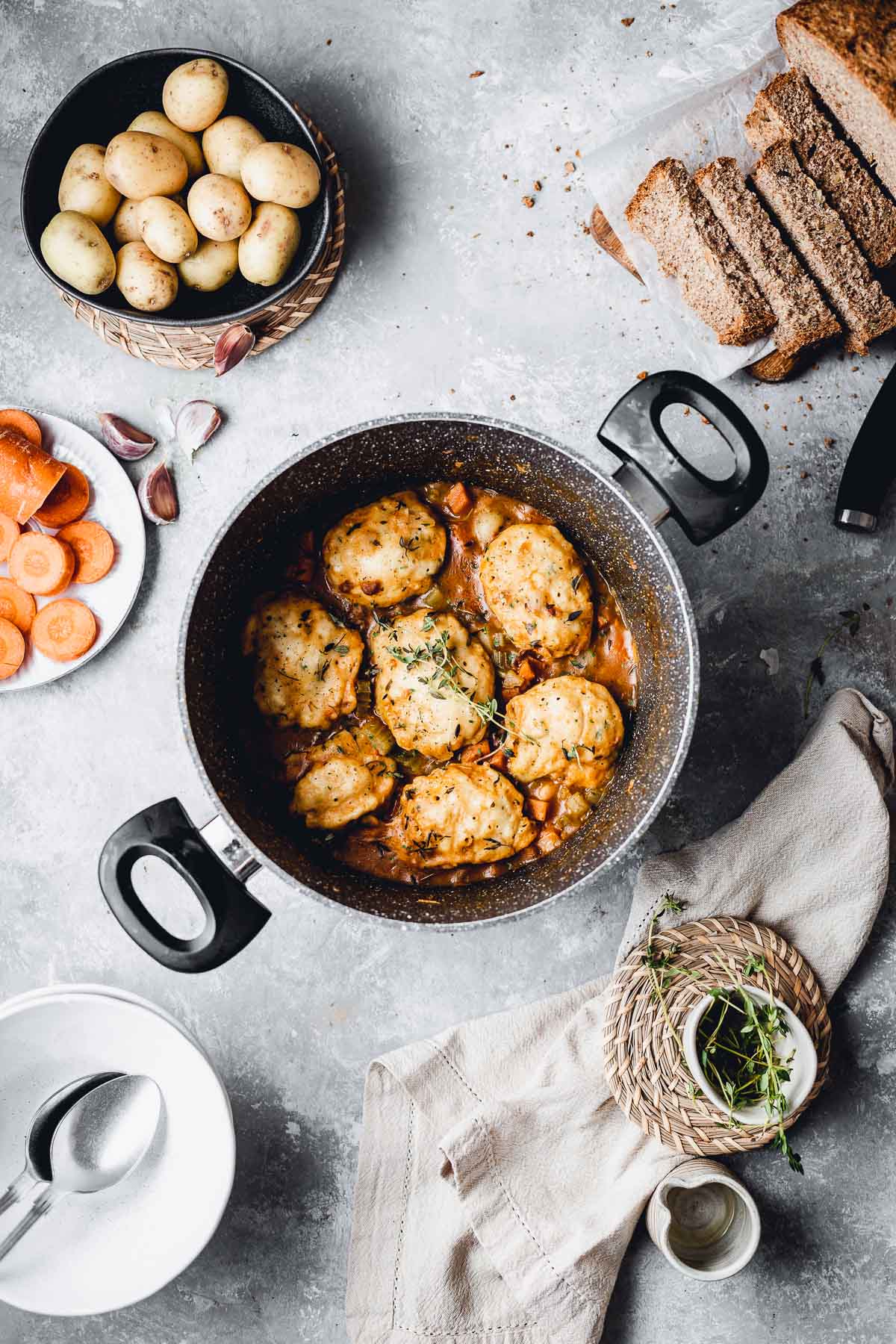 Vegetable stew in a large pan surrounded by bread, raw ingredients and toppings. 