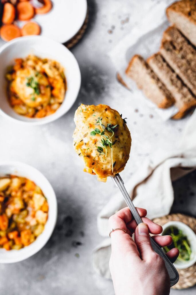 A hand holding a spoon with a vegan dumpling topped off by thyme. 