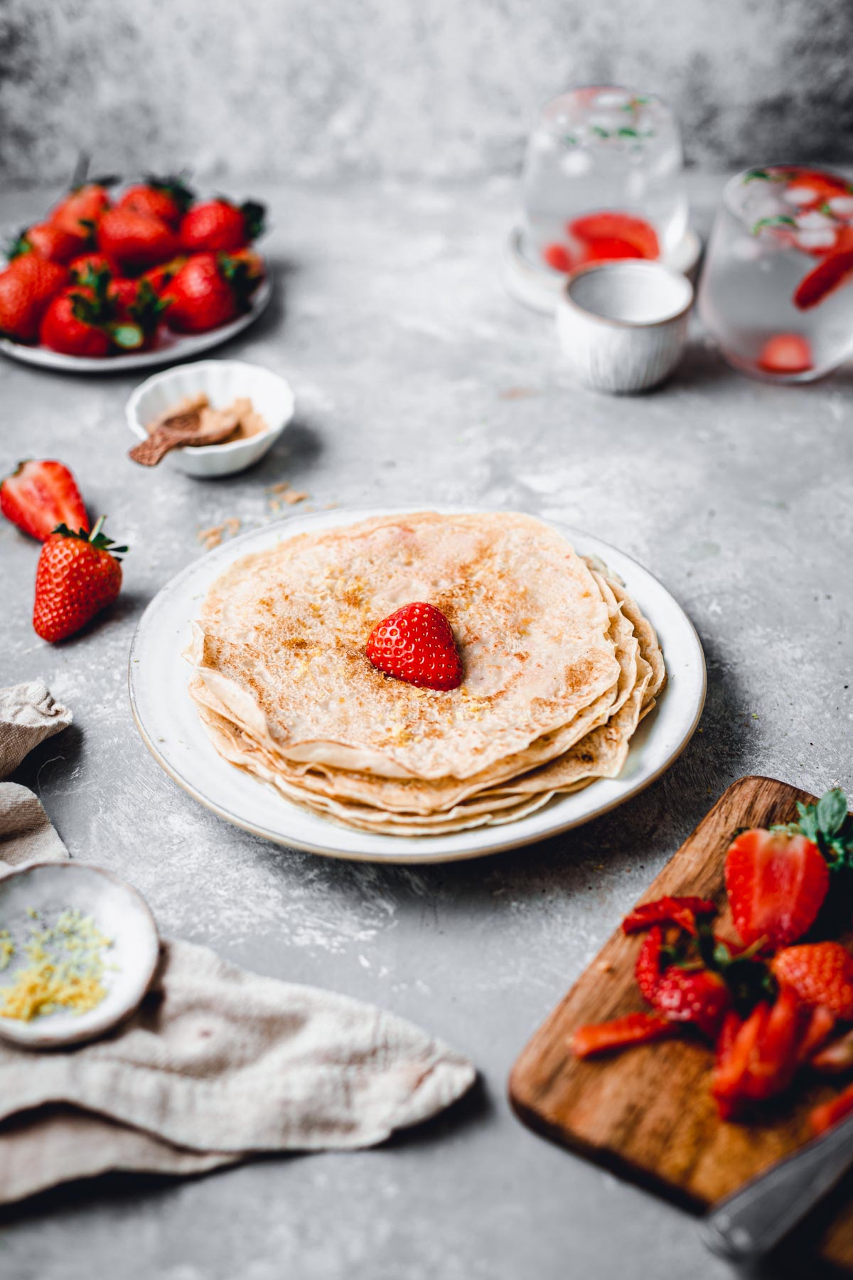 A side view of a almond milk crepes stacked on a round plate with a single strawberry on top. 