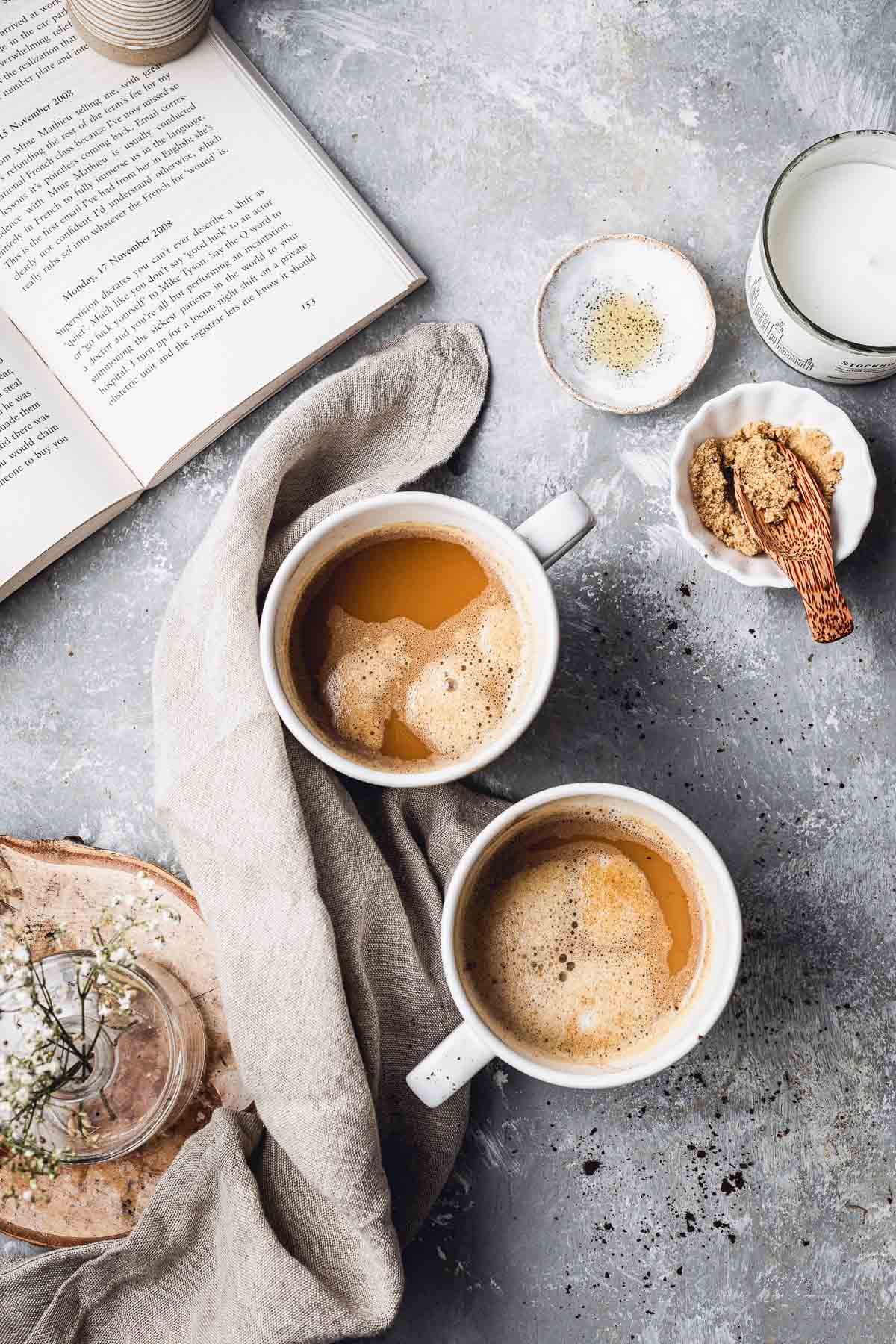 Two mugs of coffee surrounded by different small bowls. 