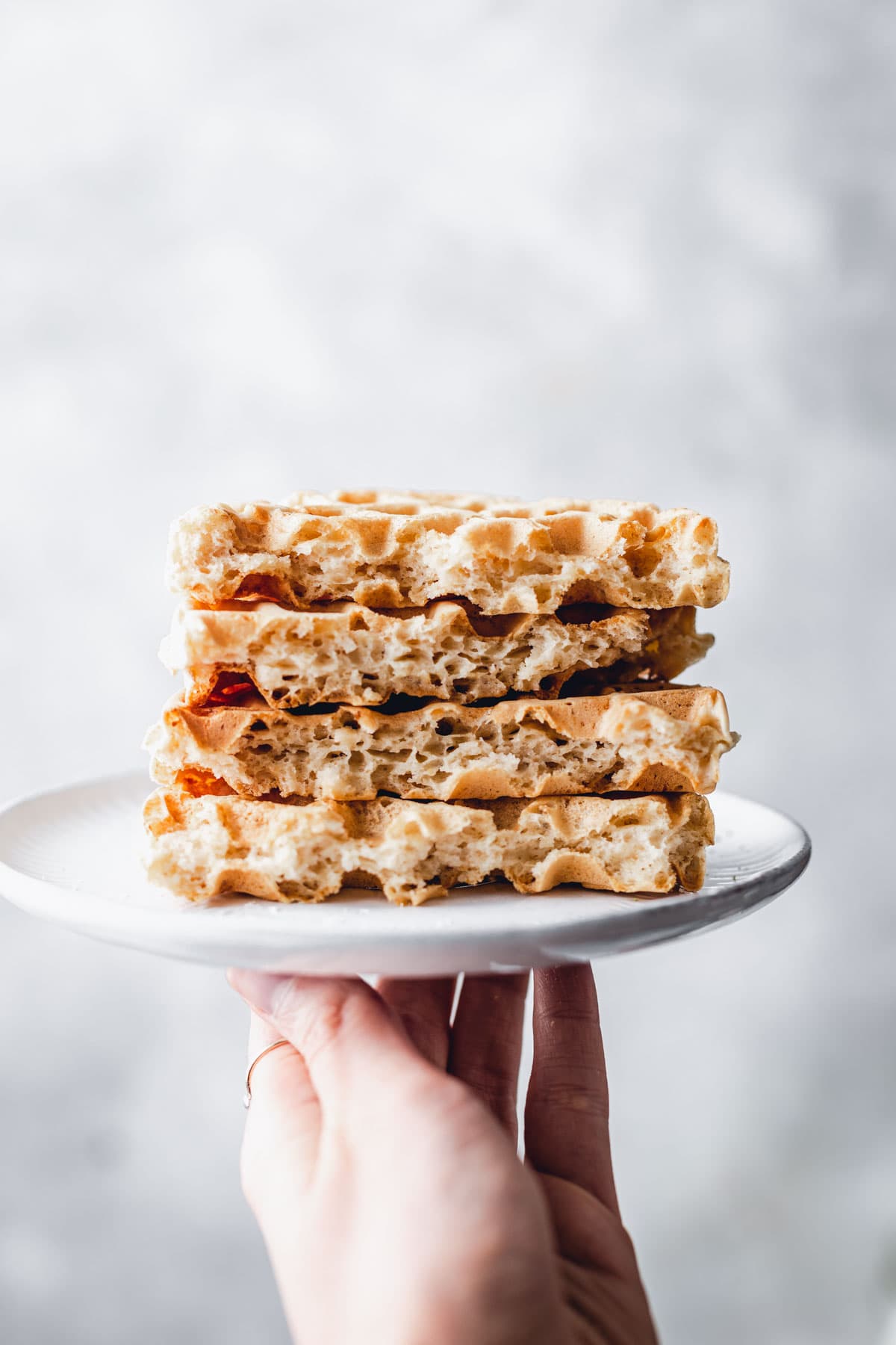 A stack of almond milk waffles on a small plate being held up by a hand. 