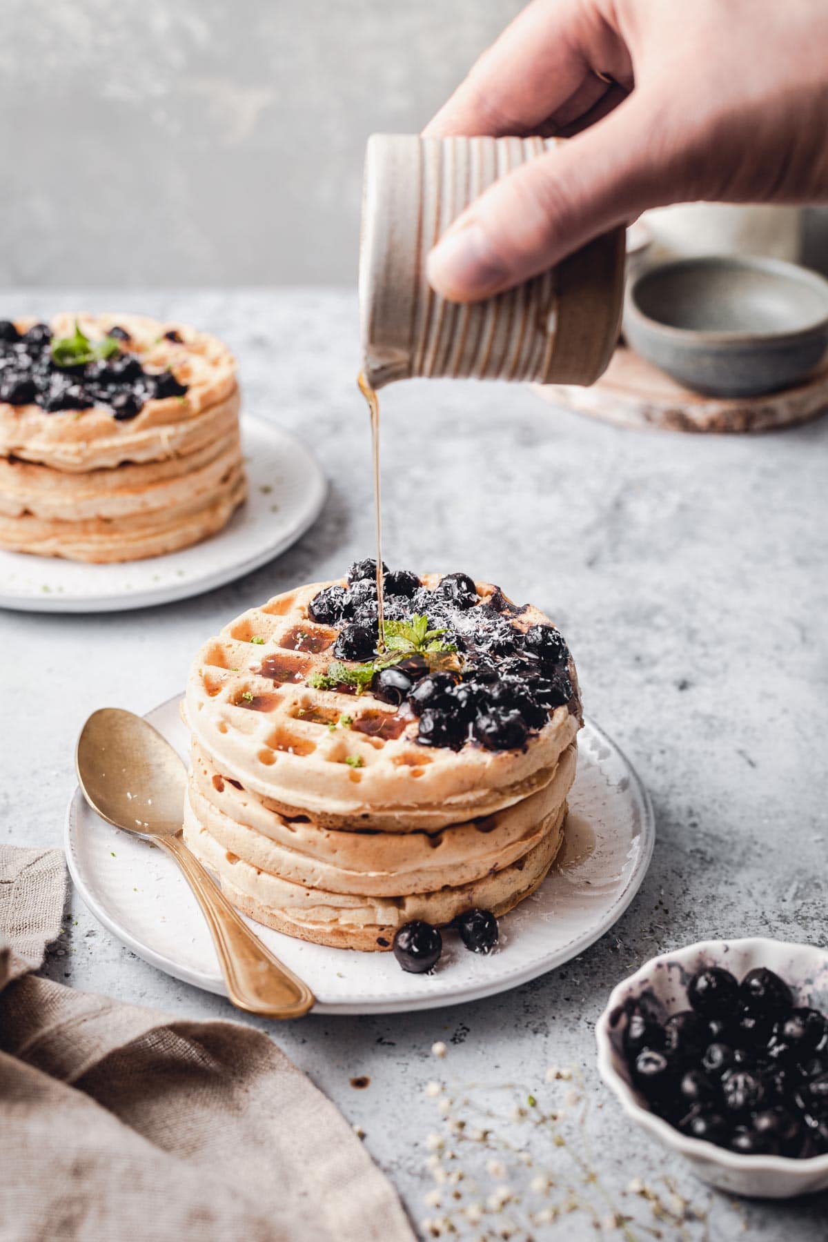 A hand pouring maple syrup over a stack of waffles. 