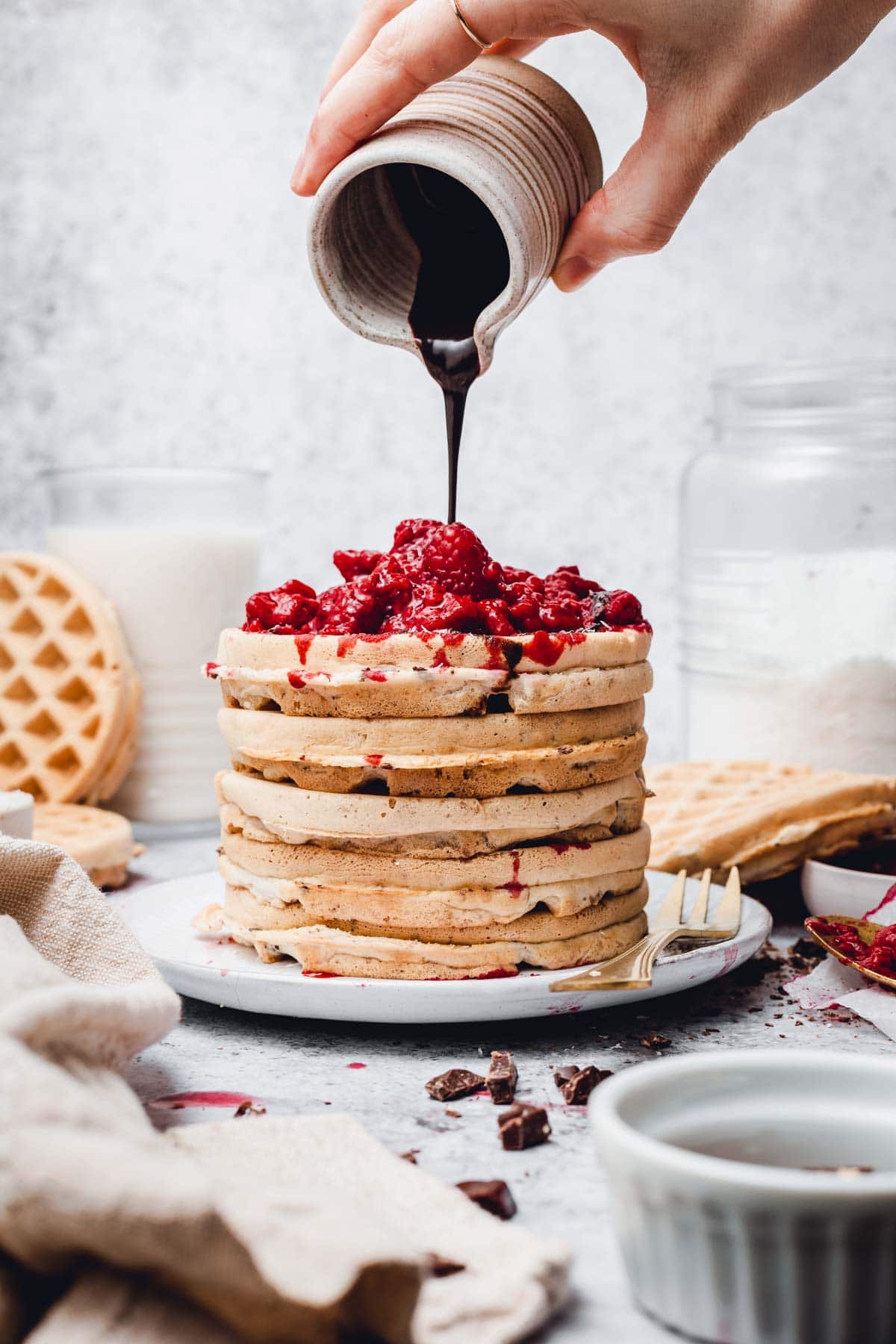 Chocolate sauce being poured over a stack of waffles.