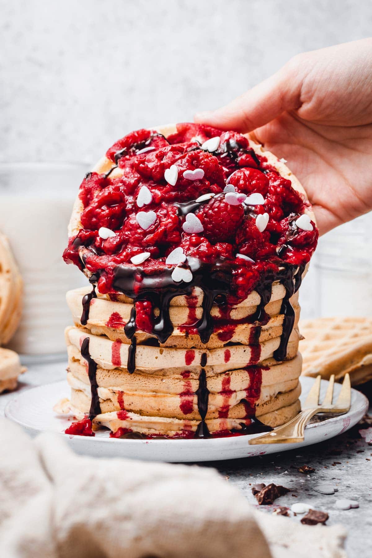 A hand reaching out to grab a stack of waffles with toppings. 
