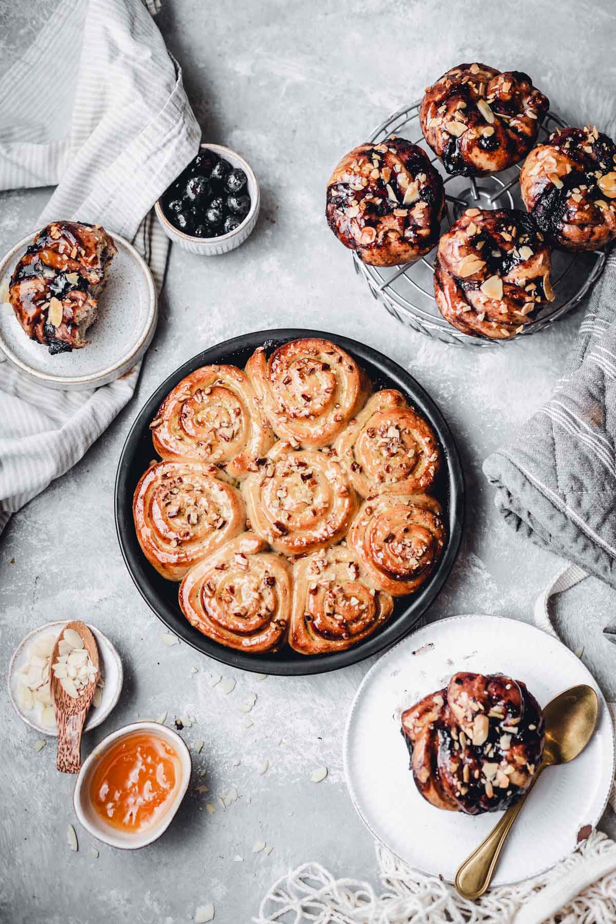 A round baking tin and cooling rack featuring various buns and breads on a flat grey surface. 