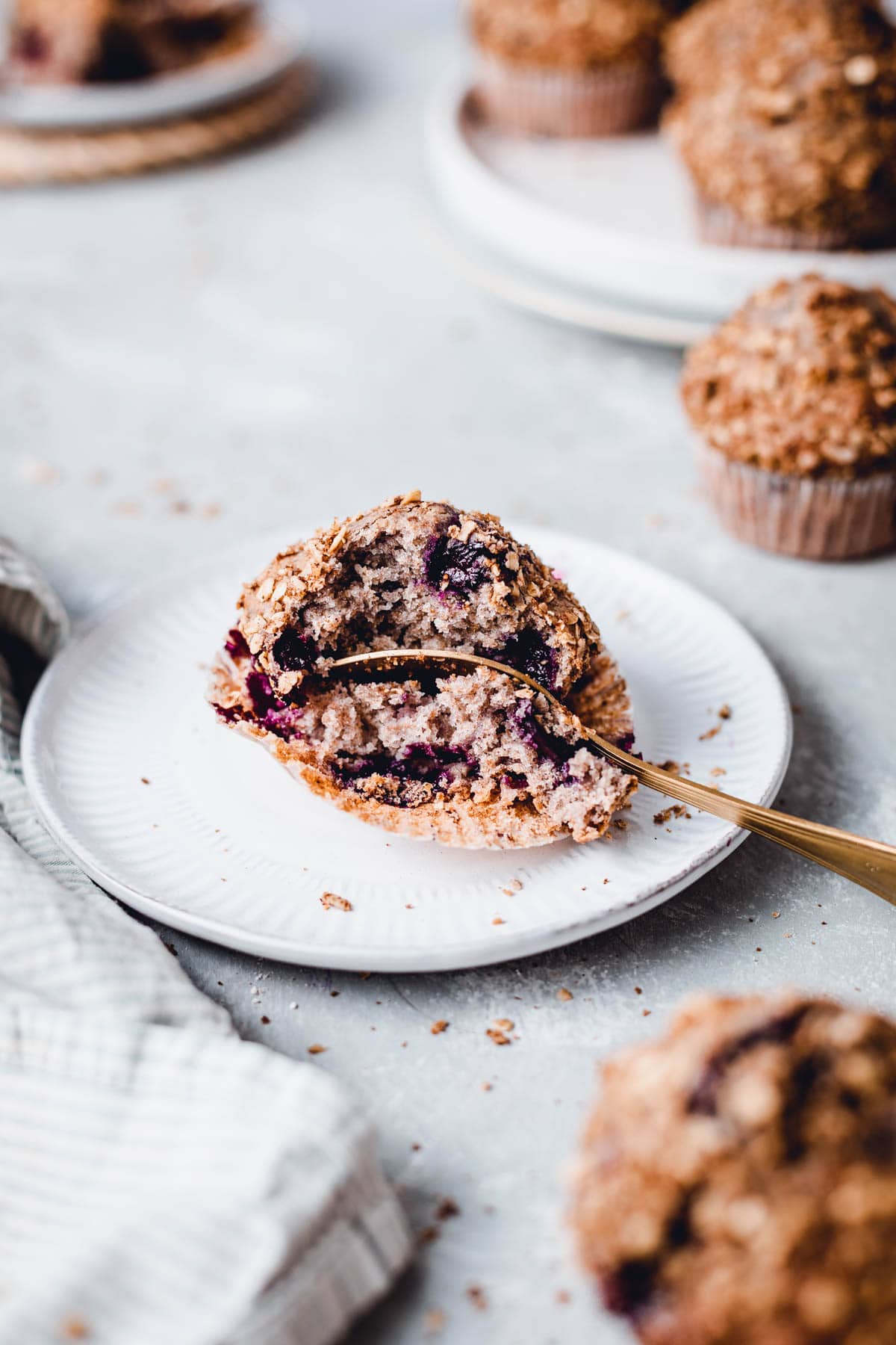 A spoon cutting into a vegan blueberry muffin on a small round plate. 