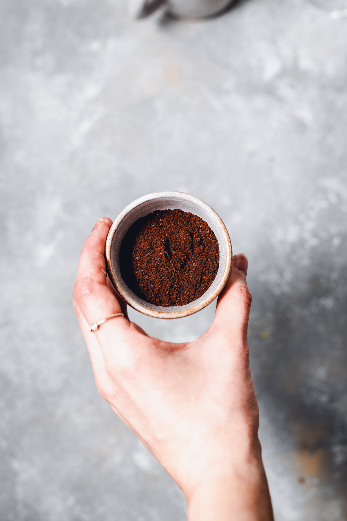 A hand holding a small bowl filled with ground coffee. 