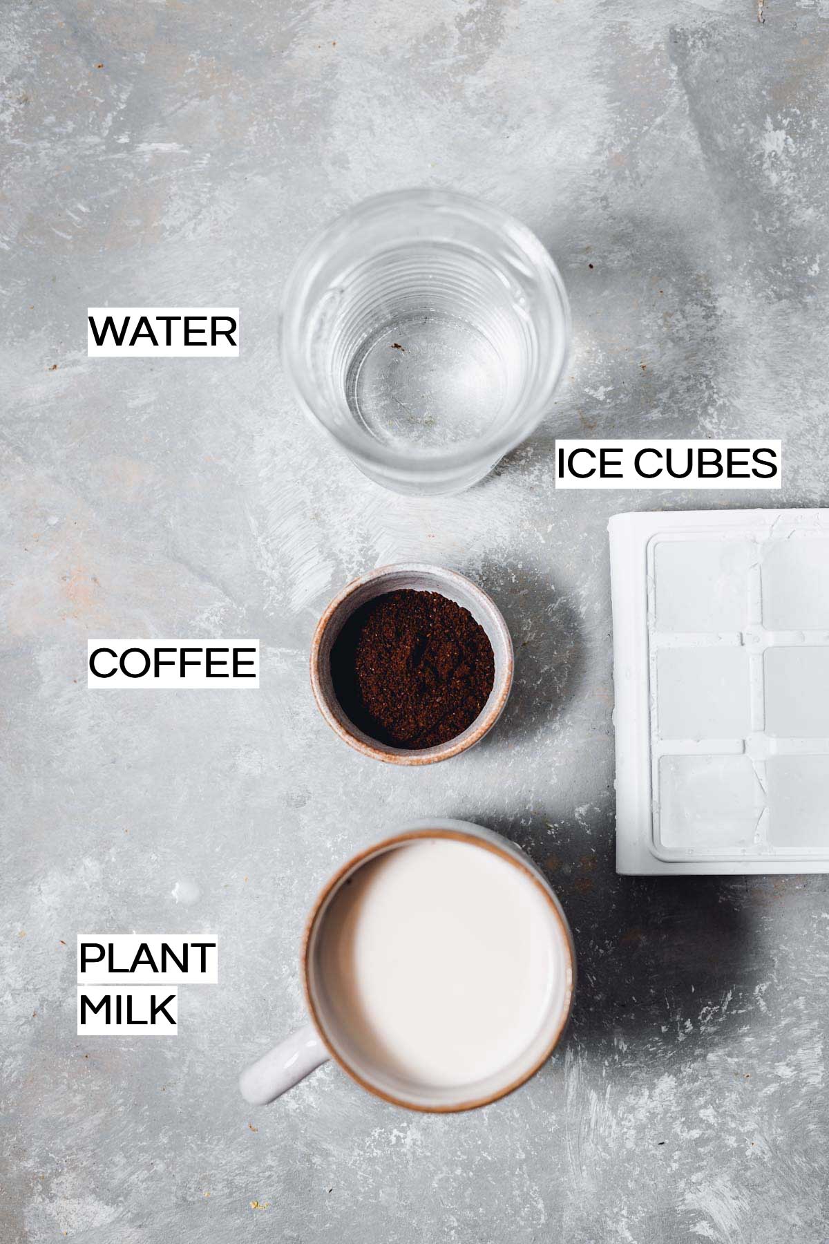 Water, coffee, plant milk and ice cubes laid out on a flat grey surface. 