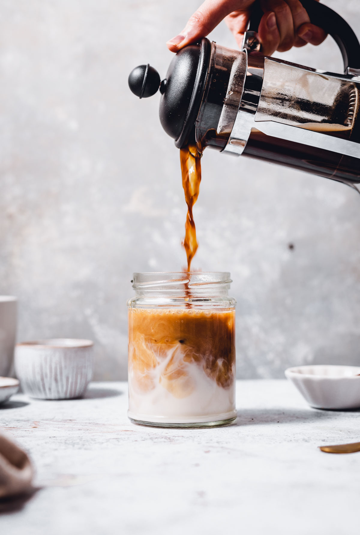 A hand pouring coffee from a French press straight into a glass. 