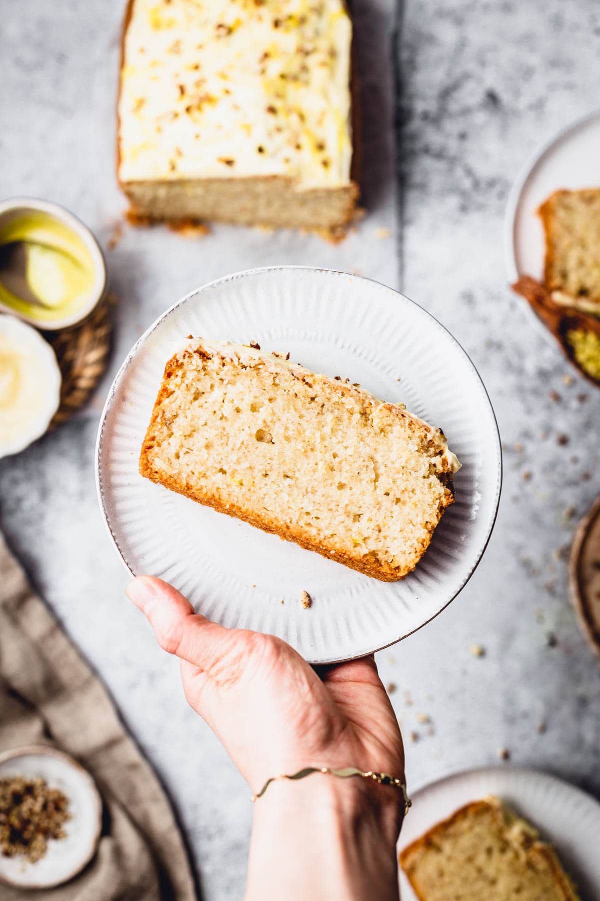 A hand holding a plate featuring a slice of lemon cake. 