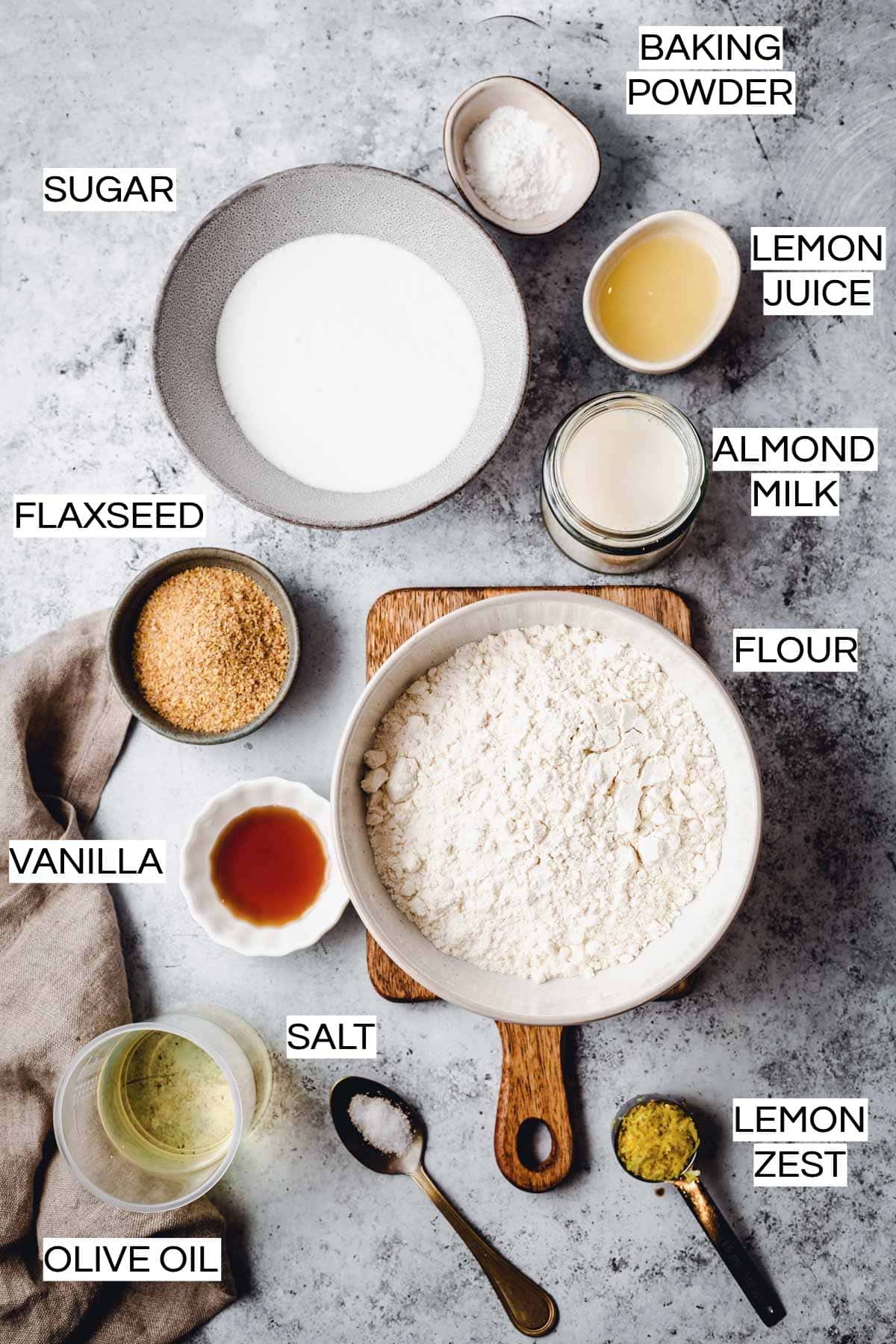 Various ingredients needed to bake a lemon cake laid out on a flat grey surface. 