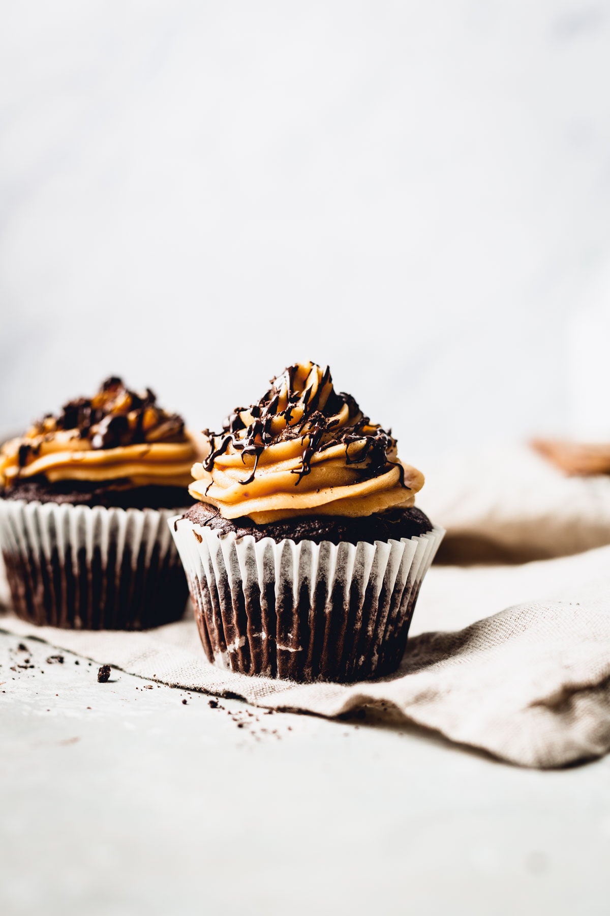 A straight-on view of two iced cupcakes drizzled with chocolate sauce. 