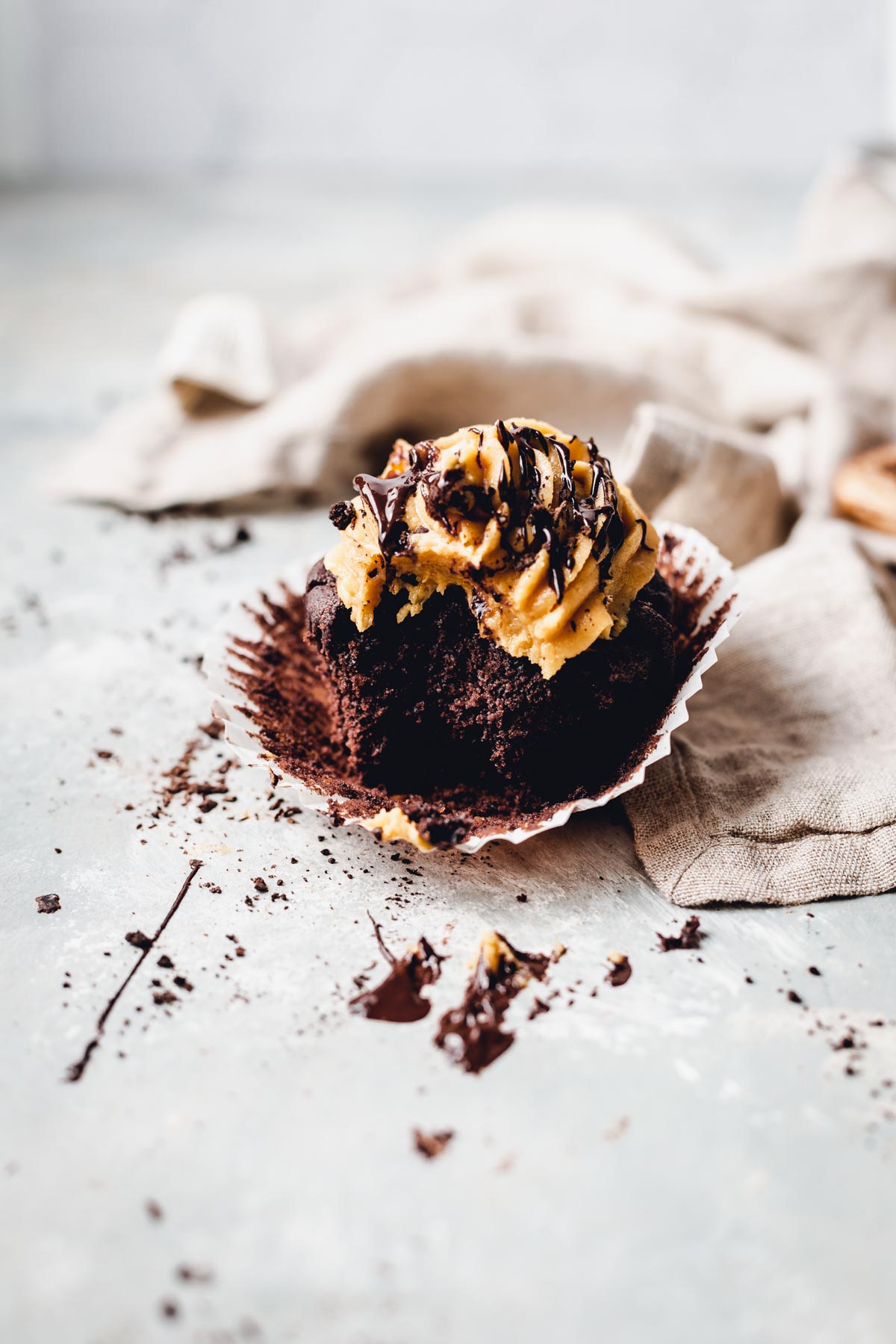 A chocolate peanut butter cupcake  with a bite taken out of it on a grey surface. 