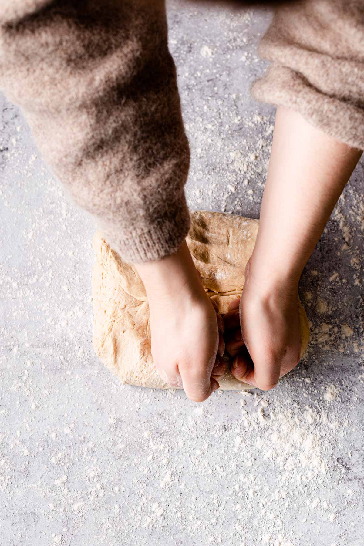 Two hands knocking back dough on a floured surface. 