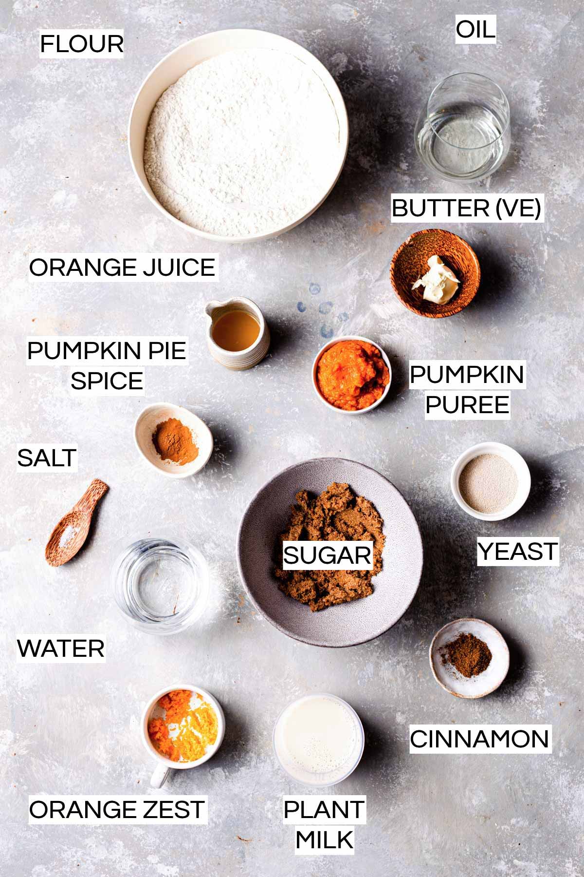 All ingredients needed to bake vegan pumpkin rolls laid out on a grey surface. 