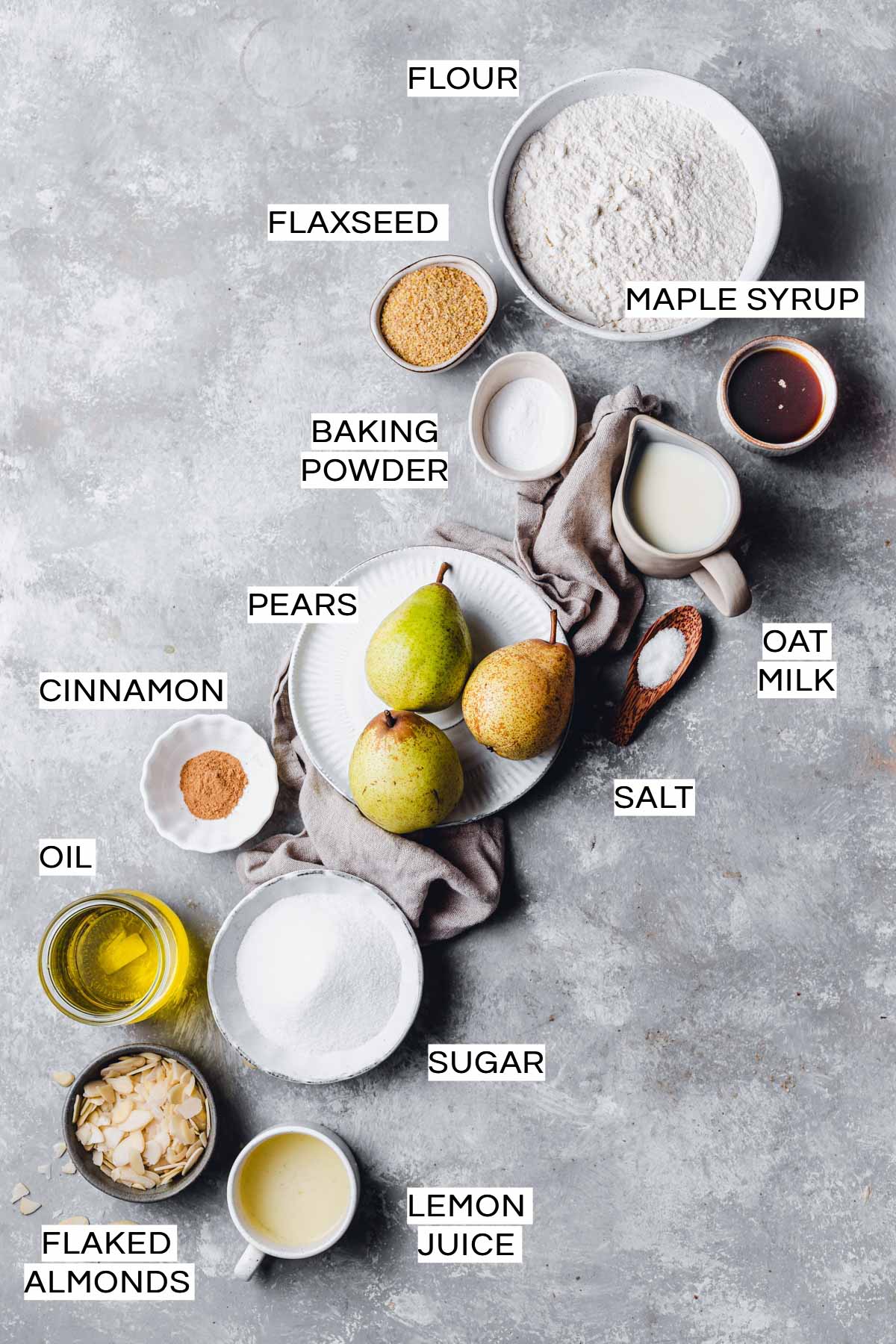 Various ingredients needed to make a vegan pear cake laid out on a grey surface. 