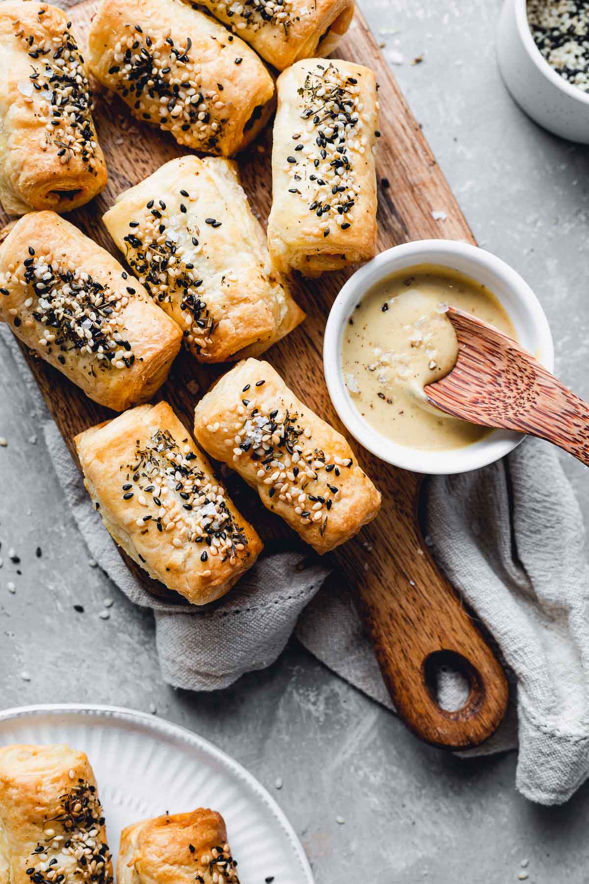 Vegan puff pastry rolls on a small wooden chopping board next to a mustard dip. 