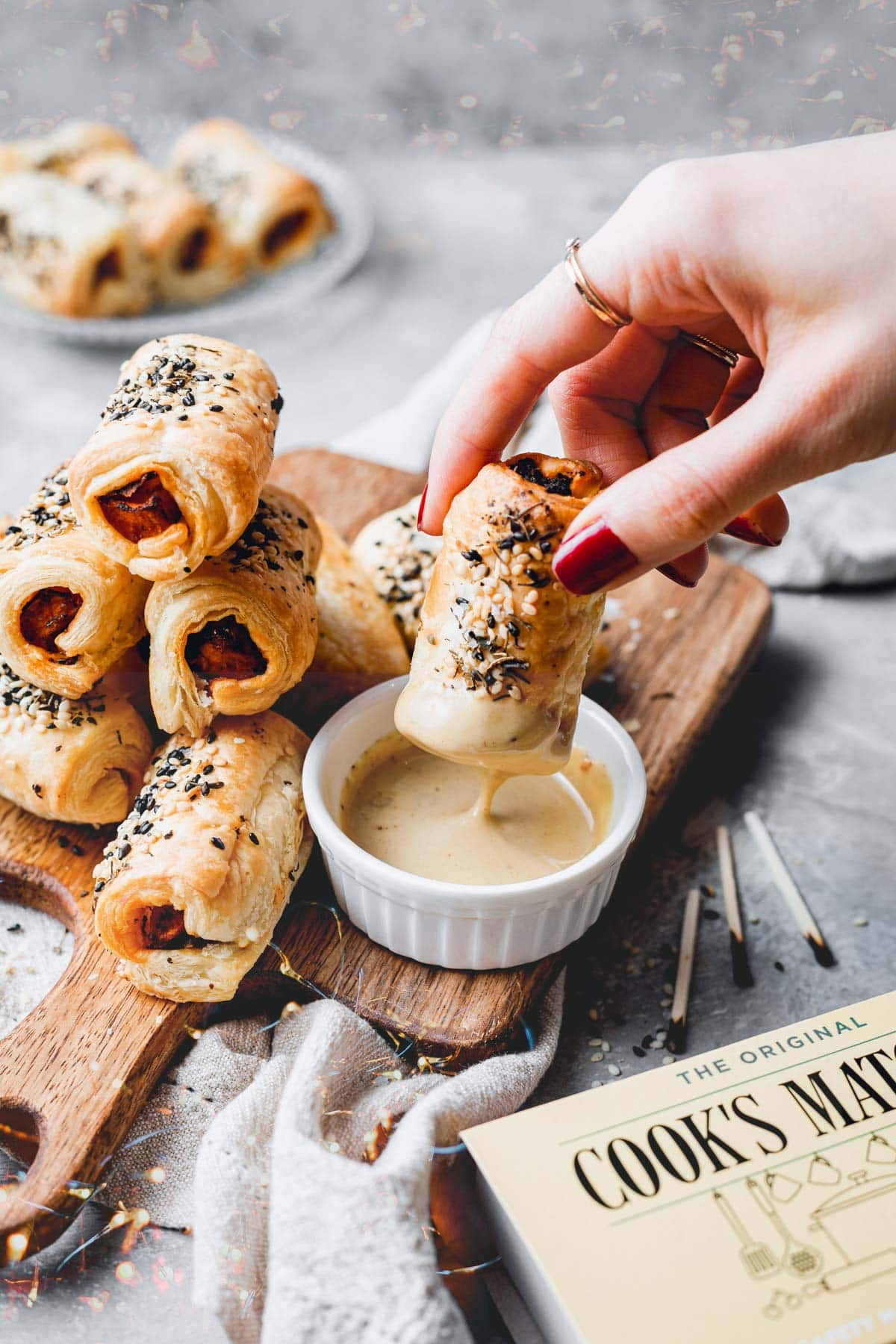 A hand dipping vegan pigs in a blanket into sauce. 