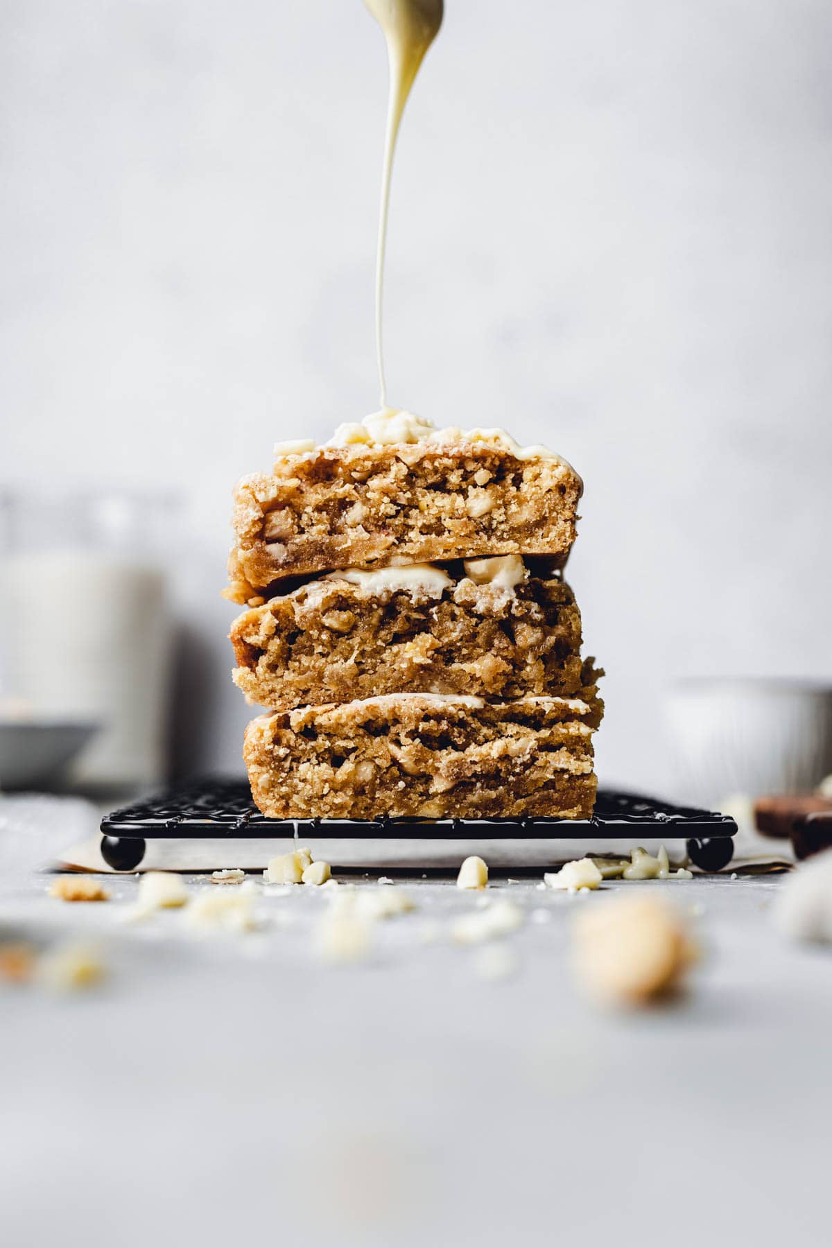 Three slices of blondie on a black cooling rack with a drizzle of white chocolate sauce coming down from the top. 