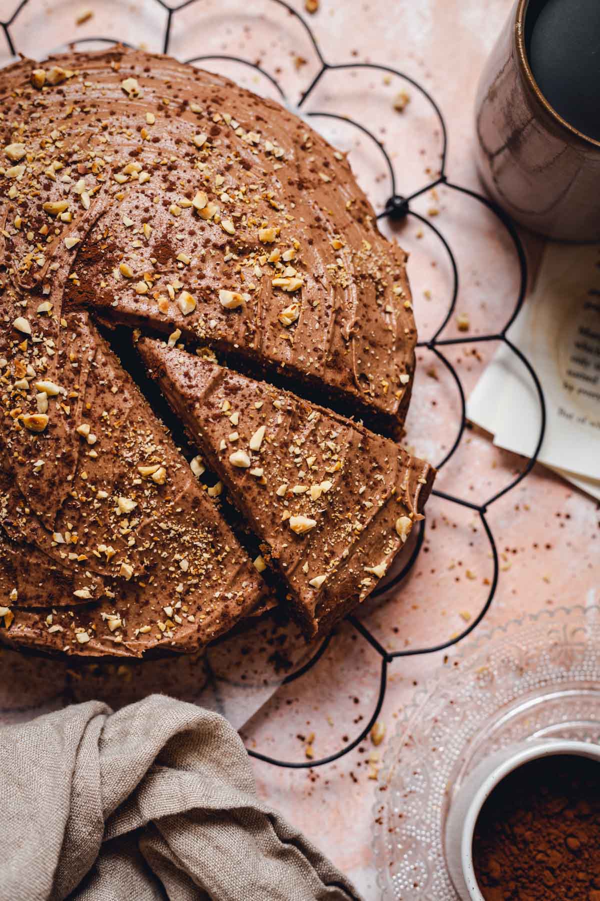 A round coffee cake placed on a black cooling rack with various objects around it. 