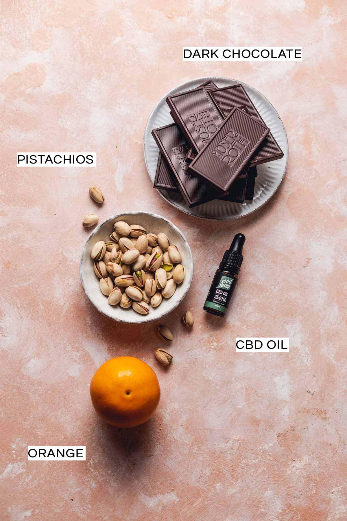 Chocolate, pistachios, orange and CBD oil placed on a flat surface. 