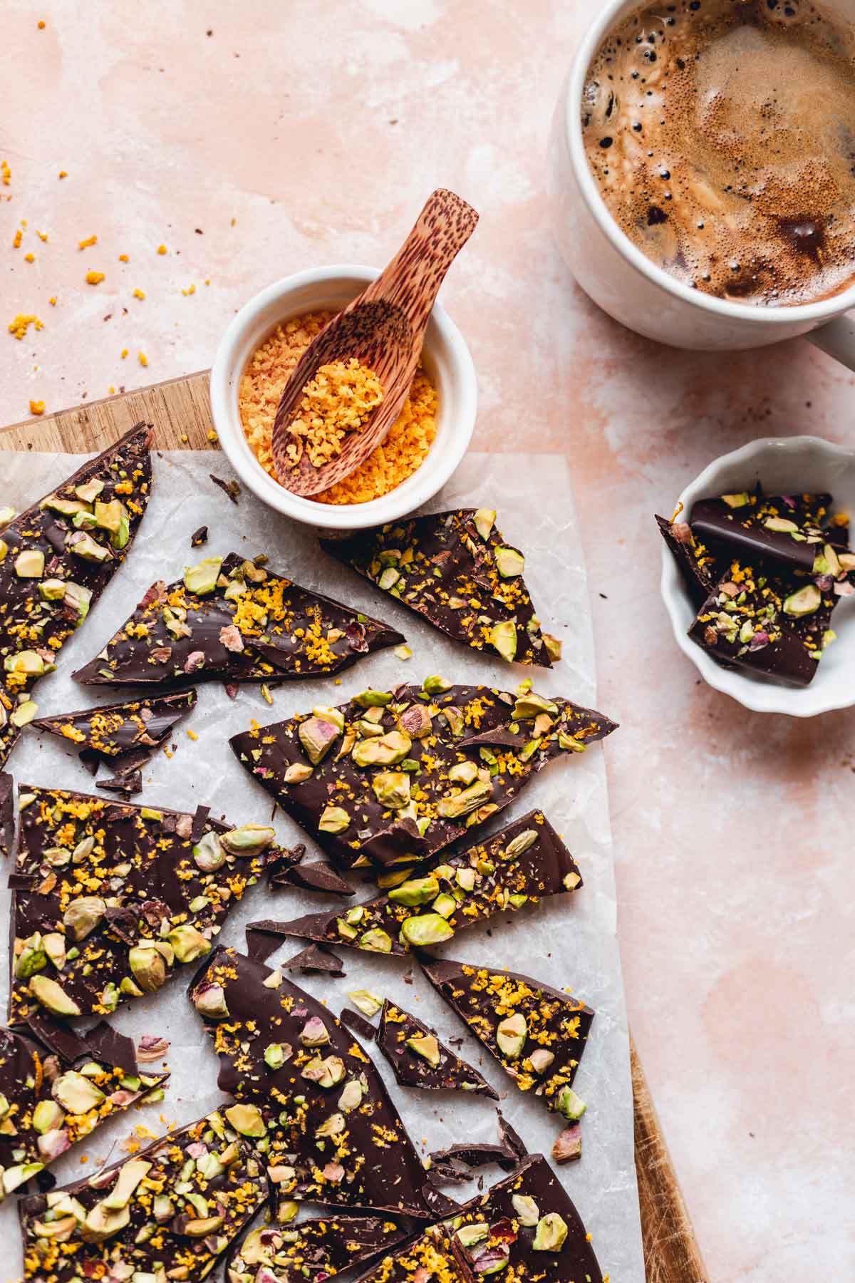 Pieces of CBD chocolate bark on white baking paper with coffee and orange zest placed next to it.
